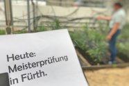 Heft mit der Aufschrift: "Heute Meisterprüfung in Fürth". Im Hintergrund Mann im Gewächshaus